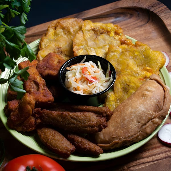 A vibrant green plate holds a variety of Plant Based Zo's vegan fried foods and a small bowl of slaw.