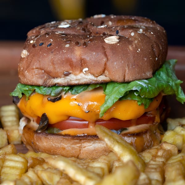 A Plant Based Zo vegan burger with melted cheese, lettuce, tomato, and sauce, surrounded by fries.