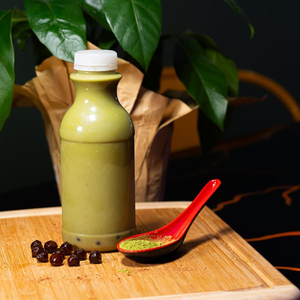A Plant Based Zo matcha drink in a bottle with boba, matcha powder, and a plant.