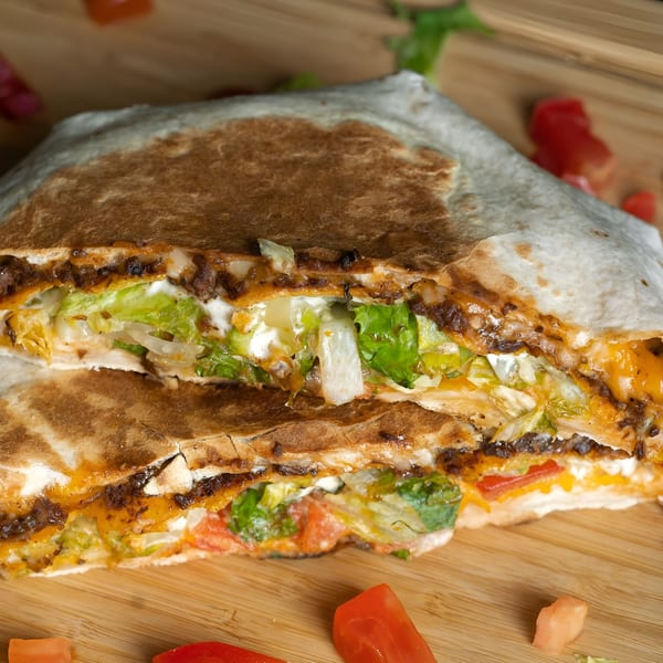 A vegan quesadilla from Plant Based Zo, cut in half, revealing lettuce, tomatoes, and cheese.